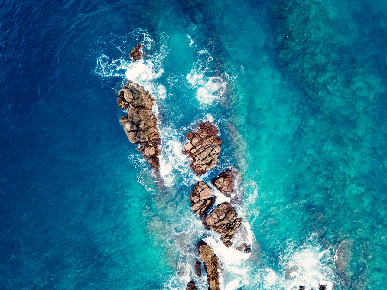 who-we-are A stunning aerial shot showcasing the vibrant blue waters and rocky coastline of Aceh, Indonesia.